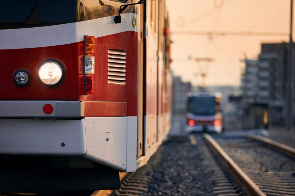 Red and white light rail train on tracks in a city at sunset