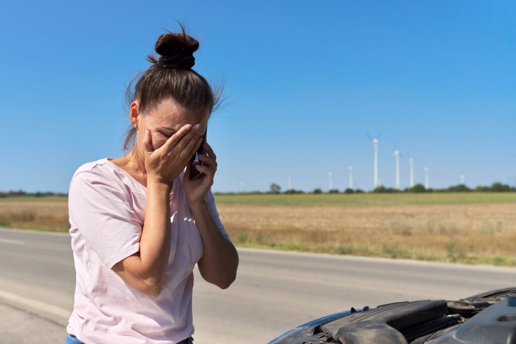 Woman on the phone by the roadside after a car accident, holding her hand over her eye